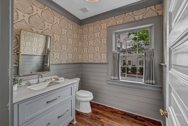 bathroom with visible vents, vanity, wood finished floors, toilet, and wallpapered walls
