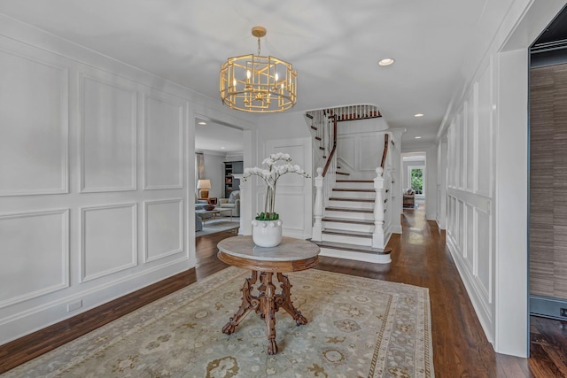 foyer entrance featuring wood finished floors, a decorative wall, stairway, recessed lighting, and a notable chandelier