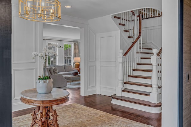 entrance foyer featuring dark wood-type flooring, stairs, a decorative wall, and a chandelier