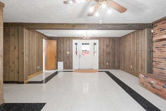 interior space with ceiling fan with notable chandelier, wooden walls, and beamed ceiling