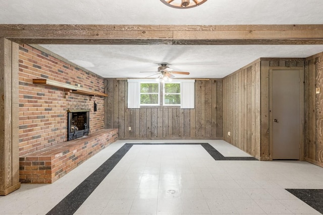 unfurnished living room with ceiling fan, beam ceiling, a fireplace, a textured ceiling, and wood walls