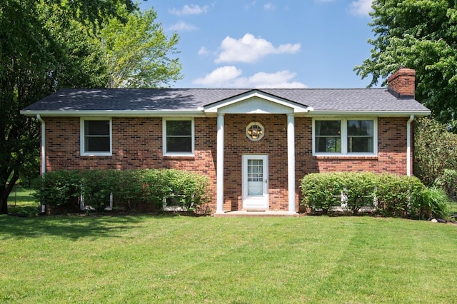 raised ranch featuring brick siding, a chimney, a shingled roof, and a front lawn