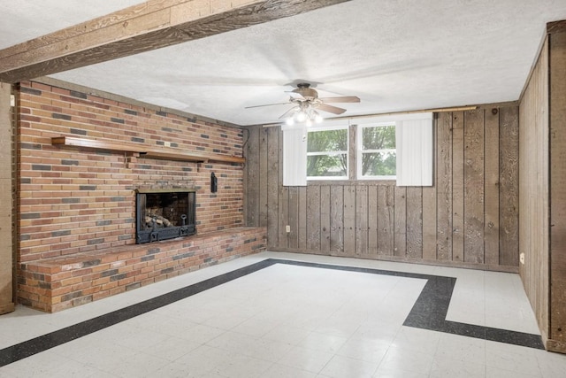 unfurnished living room featuring wooden walls, ceiling fan, a brick fireplace, a textured ceiling, and tile patterned floors