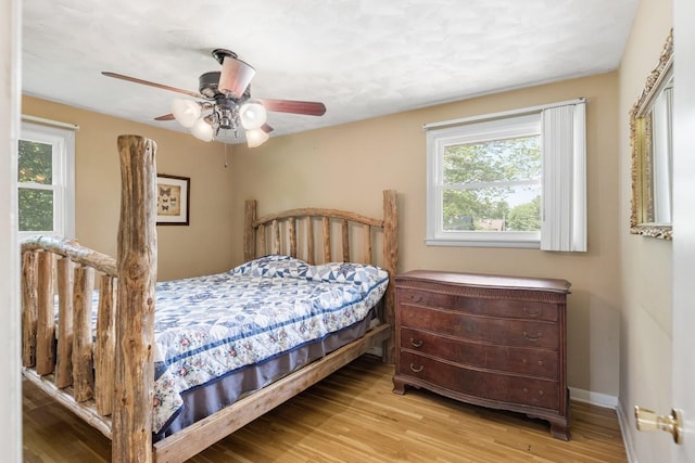 bedroom featuring baseboards, a ceiling fan, wood finished floors, and multiple windows