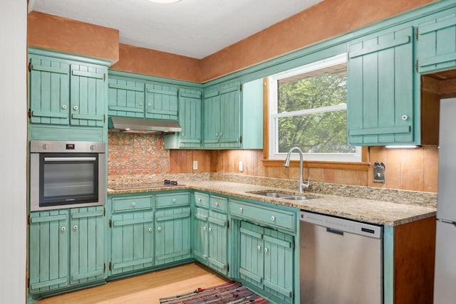 kitchen with appliances with stainless steel finishes, light wood-type flooring, a sink, light stone counters, and under cabinet range hood