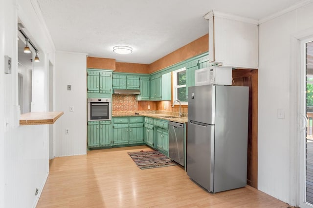 kitchen with green cabinetry, appliances with stainless steel finishes, a sink, light wood-style floors, and under cabinet range hood