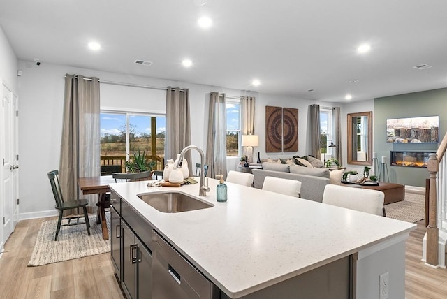kitchen with a sink, light wood finished floors, dishwasher, a glass covered fireplace, and recessed lighting