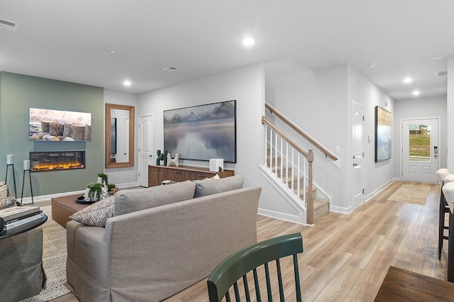 living room with stairs, recessed lighting, a glass covered fireplace, and light wood-style flooring