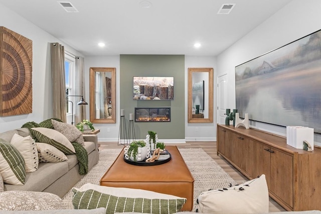 living room with baseboards, visible vents, a glass covered fireplace, and light wood-type flooring