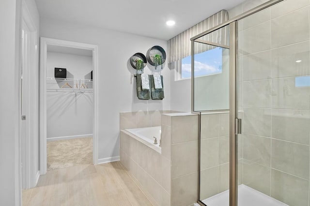 full bath featuring a garden tub, a walk in closet, wood finished floors, and a shower stall