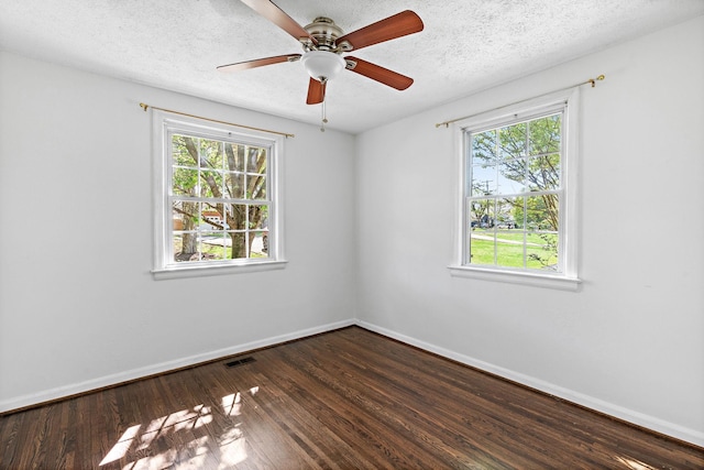 unfurnished room with ceiling fan, a textured ceiling, baseboards, dark wood-type flooring, and visible vents