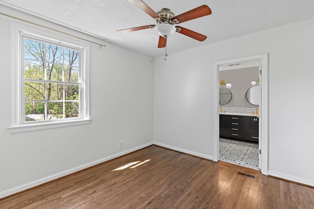 unfurnished bedroom featuring a ceiling fan, visible vents, wood finished floors, baseboards, and connected bathroom