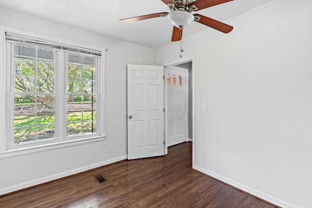 unfurnished room with baseboards, a wealth of natural light, dark wood finished floors, and visible vents