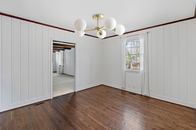 empty room featuring a chandelier, dark wood-style floors, ornamental molding, and visible vents