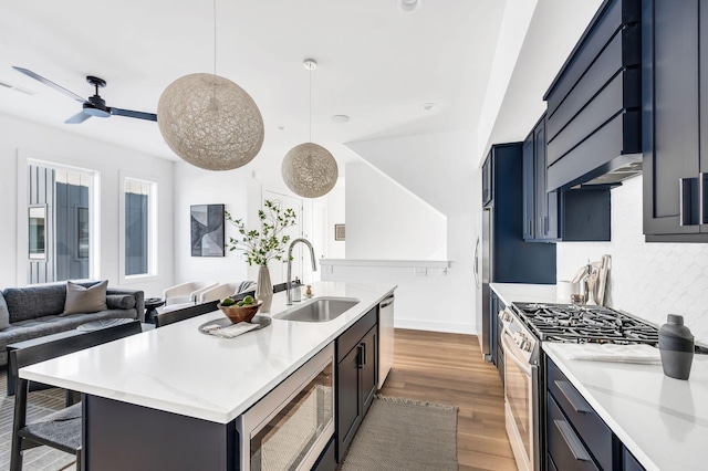 kitchen with wood finished floors, a center island with sink, a sink, backsplash, and stainless steel appliances