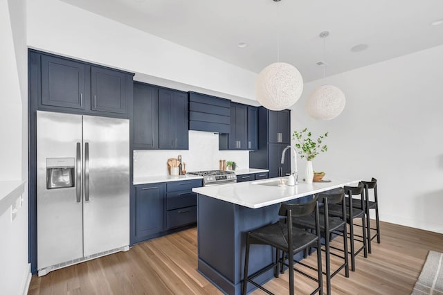 kitchen with a kitchen bar, light countertops, a sink, light wood-style flooring, and appliances with stainless steel finishes