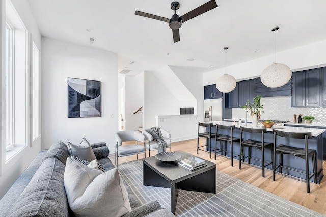 living area with stairs, a ceiling fan, and light wood-type flooring