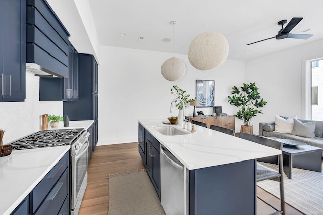 kitchen featuring a breakfast bar, gas stove, dishwasher, a kitchen island with sink, and blue cabinets