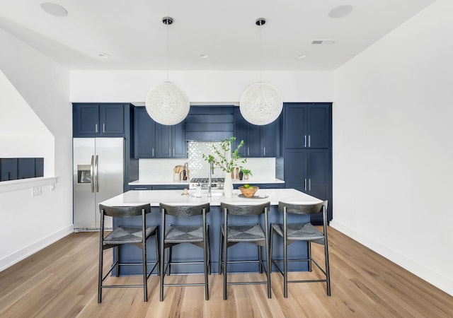 kitchen with stainless steel fridge, blue cabinets, a breakfast bar, and light countertops