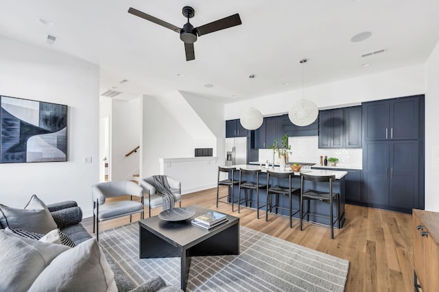 living area with visible vents, a ceiling fan, light wood-style flooring, and stairs