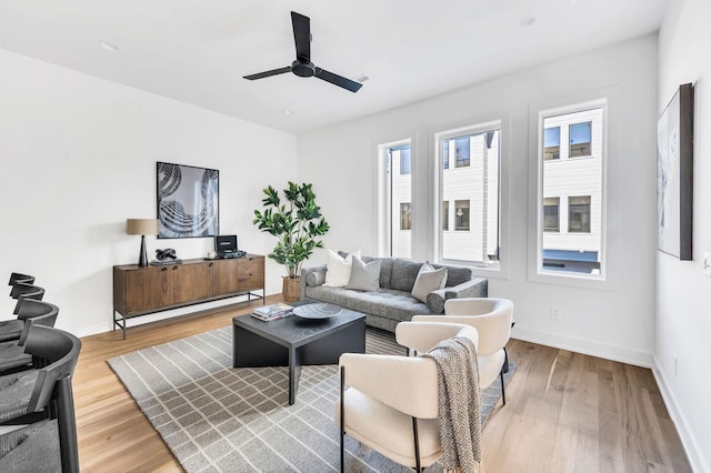 living room with light wood-style floors, a ceiling fan, and baseboards