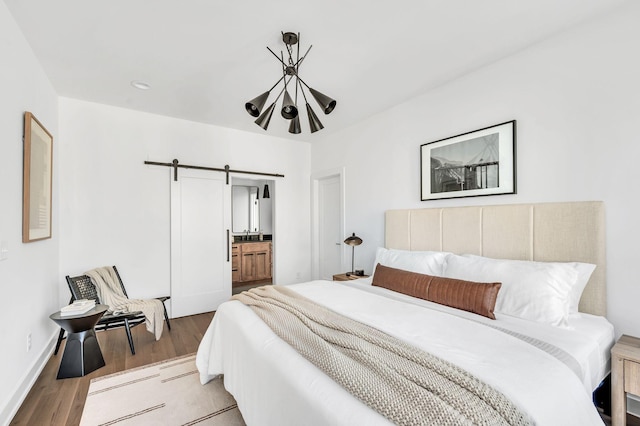 bedroom featuring a chandelier, a barn door, wood finished floors, and ensuite bath