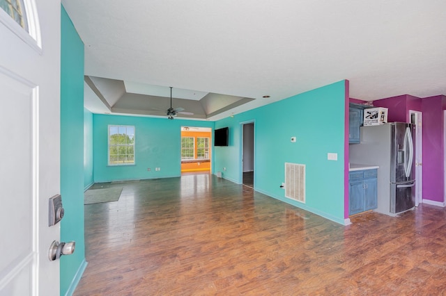 unfurnished living room with visible vents, wood finished floors, baseboards, ceiling fan, and a tray ceiling