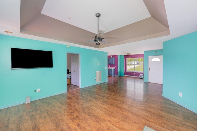 unfurnished living room with a ceiling fan, a tray ceiling, and wood finished floors