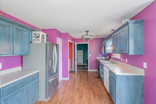kitchen featuring appliances with stainless steel finishes, a sink, light countertops, baseboards, and wood finished floors