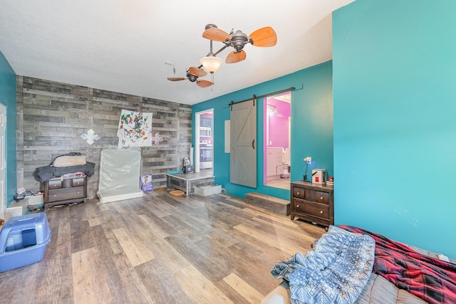 bedroom with an accent wall, a ceiling fan, a barn door, and wood finished floors