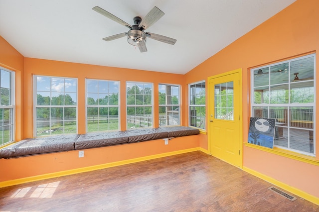 unfurnished sunroom featuring baseboards, vaulted ceiling, wood finished floors, and visible vents