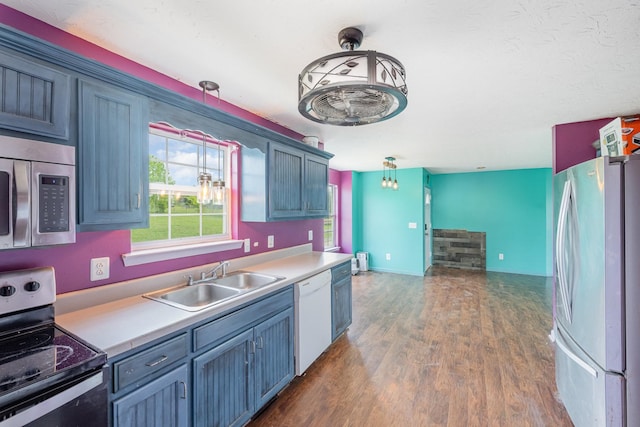 kitchen featuring appliances with stainless steel finishes, hanging light fixtures, dark wood finished floors, a sink, and light countertops