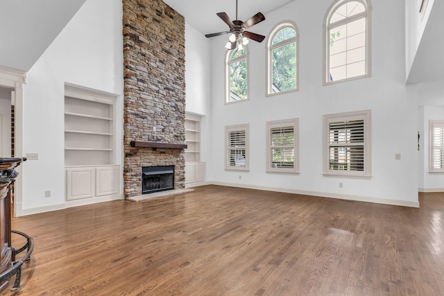 unfurnished living room with wood finished floors, ceiling fan, built in shelves, and a high ceiling