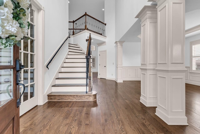 entrance foyer with a towering ceiling, decorative columns, stairs, and dark wood-type flooring