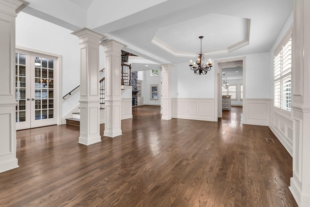 unfurnished dining area featuring a tray ceiling, french doors, an inviting chandelier, a decorative wall, and stairs