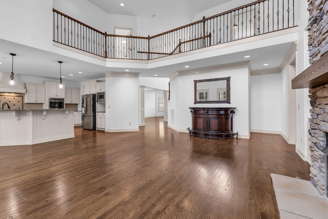 unfurnished living room featuring recessed lighting, baseboards, a towering ceiling, and dark wood-style floors