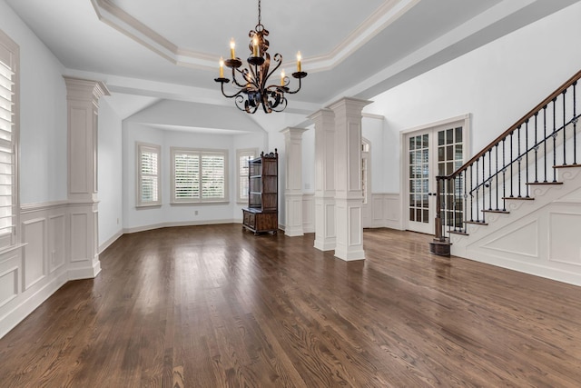 unfurnished dining area with a notable chandelier, a raised ceiling, a decorative wall, dark wood-type flooring, and stairway