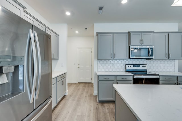 kitchen with appliances with stainless steel finishes, tasteful backsplash, light wood-type flooring, gray cabinetry, and light countertops
