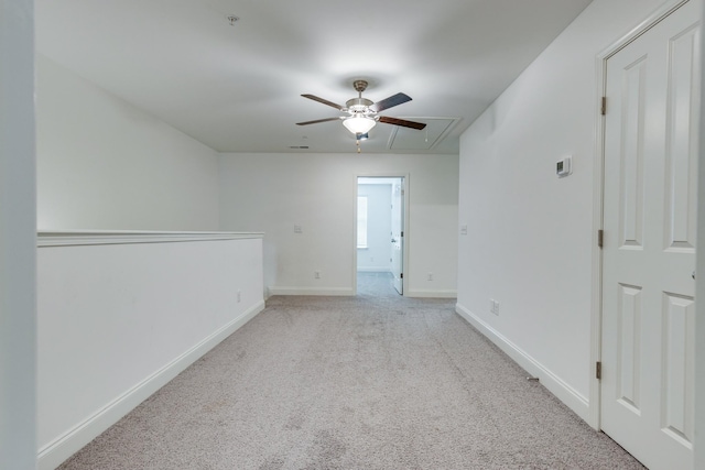 empty room with baseboards, a ceiling fan, attic access, and light carpet