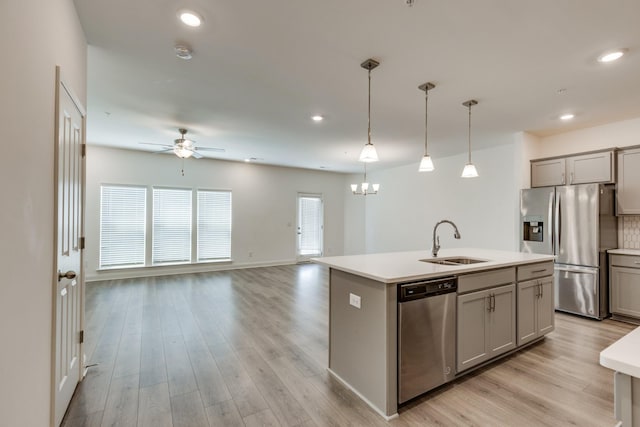 kitchen featuring appliances with stainless steel finishes, a sink, light countertops, gray cabinets, and ceiling fan with notable chandelier