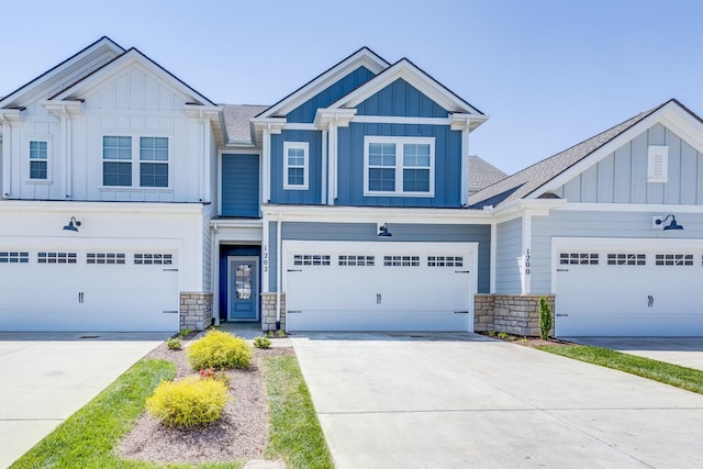 multi unit property with board and batten siding, roof with shingles, driveway, and stone siding