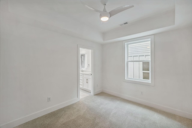 empty room featuring light colored carpet, a ceiling fan, baseboards, a tray ceiling, and visible vents