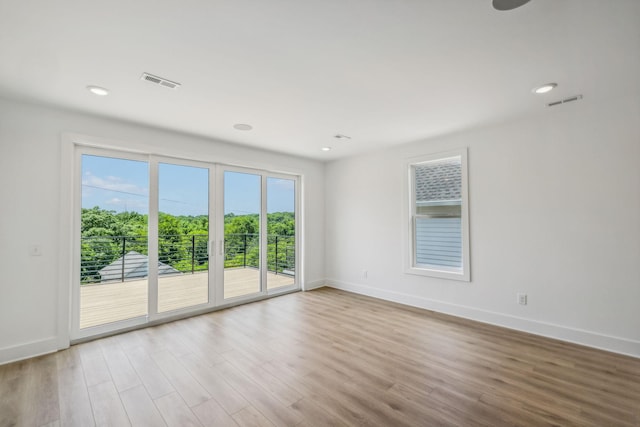 empty room featuring visible vents, baseboards, wood finished floors, and a wealth of natural light