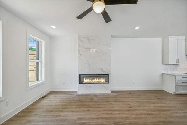 unfurnished living room with light wood-style floors, baseboards, a ceiling fan, and a premium fireplace