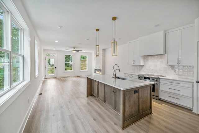 kitchen featuring light wood-style floors, white cabinetry, a sink, high end range, and backsplash