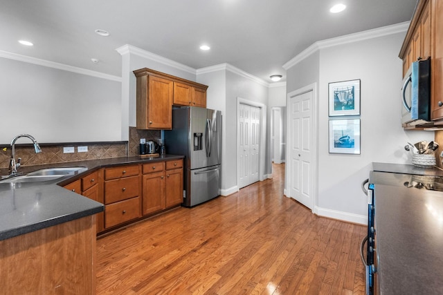 kitchen with brown cabinets, dark countertops, a sink, light wood finished floors, and stainless steel appliances