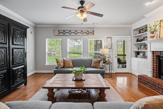 living area featuring crown molding, a brick fireplace, wood finished floors, baseboards, and a ceiling fan
