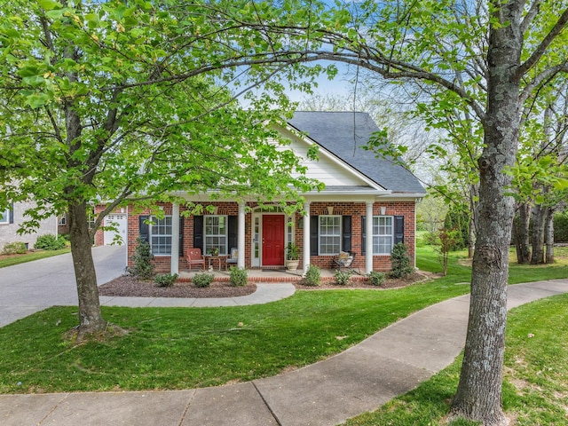 view of front of property featuring a porch, brick siding, a front yard, and roof with shingles
