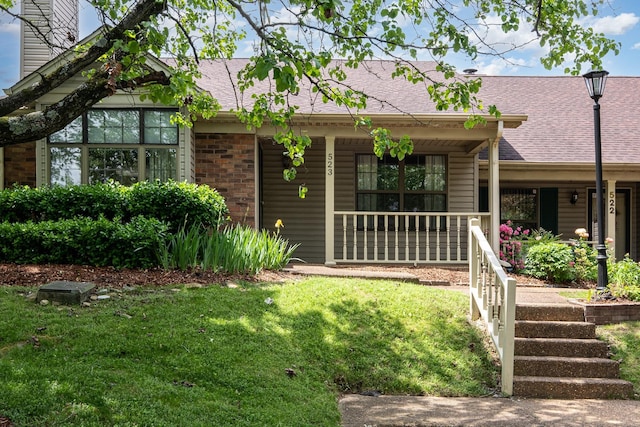 view of front of home featuring brick siding, a front lawn, roof with shingles, and covered porch