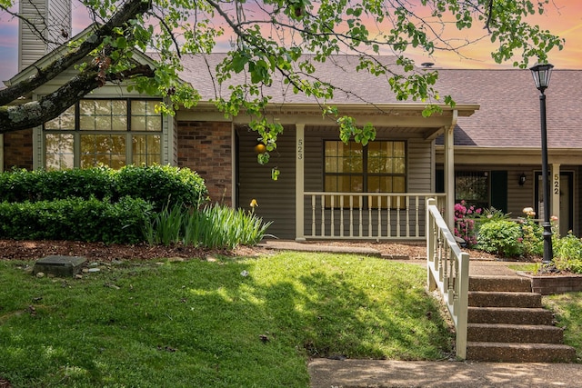 view of front of home with brick siding, a shingled roof, covered porch, and a front yard